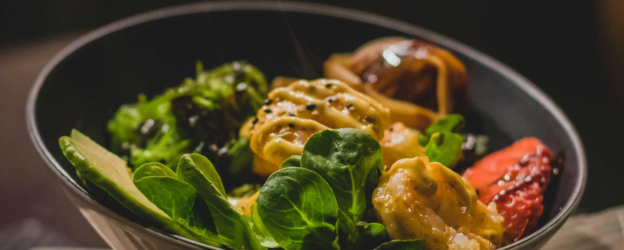 Bowl mit Feldsalat, gebratenen Garnelen in Sesam-Sauce und Avocado in einer dunklen Schale