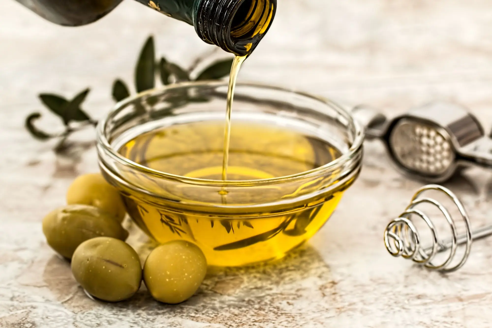 Goldenes Olivenöl wird in eine kleine Glasschale gegossen, daneben frische Oliven